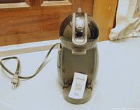 Full view of black Nescafe Dolce Gusto coffee machine with power cord visible, placed on a white surface in front of a window.