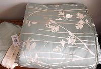 Folded queen size comforter with green base color and white floral branches pattern visible.
