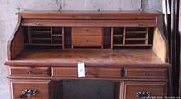 Wooden roll top secretary desk viewed from the front showing the roll top, multiple compartments, drawers, and metal handles.