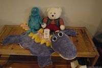 Blue dinosaur, white teddy bear, and the purple dinosaur rug all positioned on a wooden surface