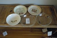 Photo of 2 clear Pyrex pie plates, 2 ceramic apple pie pie plates, and 1 small bowl on wooden surface