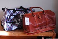 Both travel bags shown side by side on table; tan Ellen Tracy bag and plaid Olympia bag
