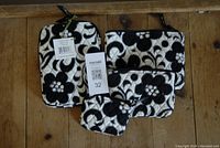 Four Vera Bradley fabric items featuring the Day and Night pattern laid out on a wooden surface, including the e-reader sleeve with tags and three zippered cosmetic bags.