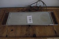 Front view of vintage electric hot plate on wooden surface, showing rectangular metal surface with control knob and power cord.