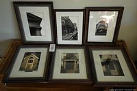 Four framed black and white photographs displayed side by side, showing architectural elements such as columns, facades, and doors. Frames show scratches.