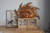 Photo shows all four wall art pieces together: large metal sun, metal butterfly, and the two butterfly shadow boxes on a wooden surface against a white wall.
