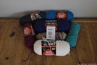 Overview of all yarn skeins including black, dark blue, maroon, white, multicolor, and teal colors