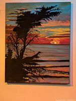 Frontal photo of the sunrise painting showing tree silhouette and vibrant sky colors.