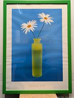 Two identical framed prints showing yellow vase with daisies on blue background by Masao Ota in green frames