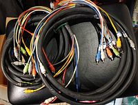 Two coiled, thick black RCA-to-RCA audio snakes with colour coded connectors visible, photographed together on a black surface.