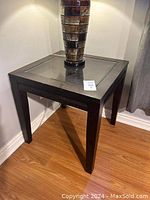 Full view of the cappuccino brown wooden end table with glass insert top, standing on wooden floor beneath corner walls.