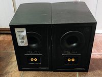 Rear view of two Infinity Beta 10 speakers showing horn tweeters, speaker terminals, black wood finish, and some scratches.