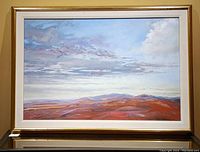 Framed oil painting showing landscape with reddish hills and cloudy sky