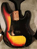 Japanese Precision Bass style guitar body with sunburst finish and black pickguard seen frontally showing wear and screw holes.