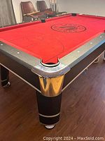 Corner view of pool table showing black frame, chrome corner protector, red felt and pocket