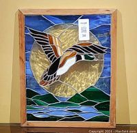 Full view of stained glass art piece showing a mallard duck flying against a blue and yellow background in a wood frame.