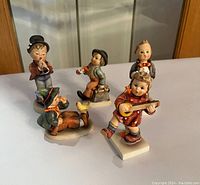 Photo showing all five Hummel & Goebel porcelain figurines arranged on a white surface for overview.