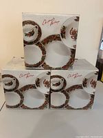 Three cardboard boxes with Christmas Heritage 20-piece dinner sets shown on box art with holiday-themed plates and cups.