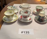Front view of six teacups and saucers on a table, showing floral and colorful patterns.