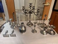 Group view of the pewter candelabra, various candle holders, and the vase arranged on a white surface in front of a glass door.