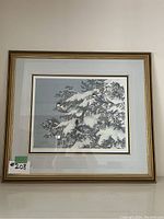 Framed signed and numbered winter pine tree print by Christine Marshall, shot front-on against a wall.