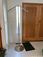 Full view of tall metal coat rack with round base, missing finial at top, near wood doors.