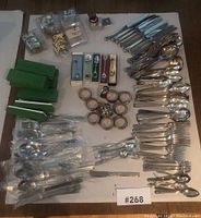 Top-down view of assorted cutlery, boxed spoon sets, napkin rings, and serving utensils arranged on a flat surface.