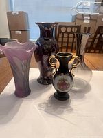 Four decorative vases arranged on table, showing shapes and colors: purple ruffled-edge, tall purple, black Limoges-style, clear/grayscale glass.