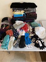 Overview of large lot of mitts, hats, scarves, gloves arranged on table with visible tags and folded scarves