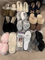 Top-down photo showing 12 pairs of slippers and socks assorted in rows on carpet, featuring various brands and styles, mostly light and neutral colors with some black and pink items.
