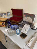 Wide view of the table showing all items including the wooden silverware box, decorative plates, glass dish, vases, wooden and trinket boxes, and boxed collectible plates.