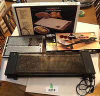 View of the three vintage Salton electric hot trays with their original boxes on a wooden table, showing the front and top surfaces of the trays.