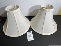 Two white fabric lamp shades placed side by side on black surface with white background, showing overall shape and condition.