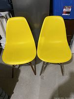Front view of two yellow Eiffel style dining chairs with wooden legs wrapped in plastic