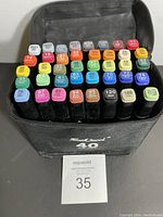 Top view of the 40 artist markers standing upright in a black zippered fabric case, showing the color-coded caps with numbers and shades across a variety of colors.
