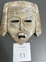 Front view of alabaster mask showing carved details and openings for eyes and mouth