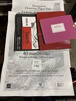 Photo showing a newsprint drawing paper pad, a Canson sketch pad, and three spiral bound sketch books in black, red, and purple, displaying the variety of artist drawing pads and sketch books.