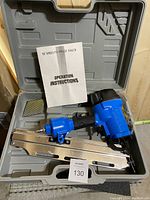 Blue QZ Series pneumatic framing nailer in a molded gray plastic carrying case with operation instructions booklet and strip of nails.