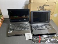 Photo showing front view of both laptops open, Acer Aspire One on left and ITSHOO laptop on right with carrying case underneath.