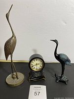 The lot showing two bronze bird figurines and an antique mantel clock on a black surface.