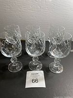 Front view of six crystal wine glasses with diamond cut pattern on a black surface.