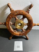 Top view of wooden boat wheel showing eight handles, brass center hub, and scratches from storage