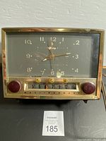 Front view of the vintage Westinghouse clock radio showing the clock face with brass frame, hour markers, hands and three gold control knobs below the radio dial.