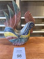 Front-angle side view of wooden rooster figurine showing the colorful paint and detailed feathers.