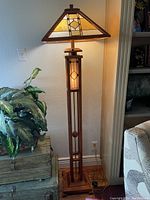 Lamp illuminated, showing stained glass shade and wooden mission-style base.