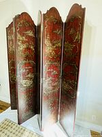 Full view of the 6-panel folding screen showing red wood panels with detailed gold handprinted traditional Chinese landscape designs.