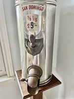 Photo showing metallic cylindrical body of the coffee grinder with a 'San Domingo' label and dispensing spout on wood base.