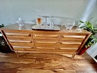 Front view of mid-century modern wooden credenza with 9 drawers standing on angled legs. Shows the wood finish and drawer design.