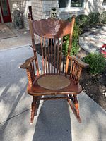 Photo of a late 1800s Victorian wooden rocking chair with carved details and spindle supports in outdoor lighting.