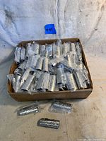 Box filled with multiple individually plastic-wrapped silver-tone metal lighter covers showing embossed horse designs.